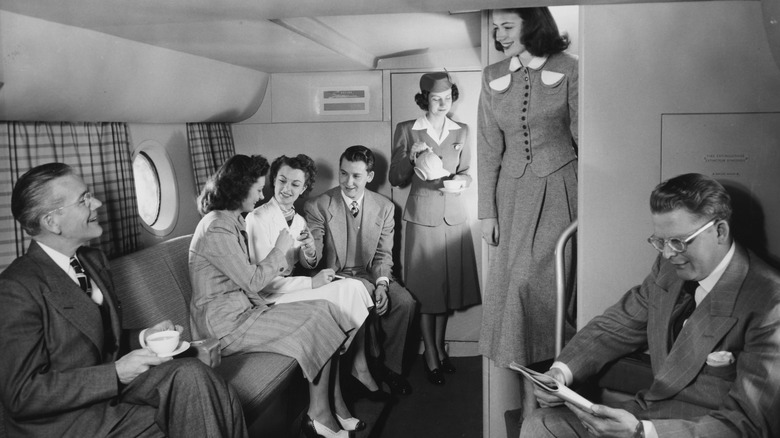An air stewardess pours a hot drink as passengers relax in the lower deck lounge of a Pan American Airways Boeing 377 Stratocruiser, circa 1950.