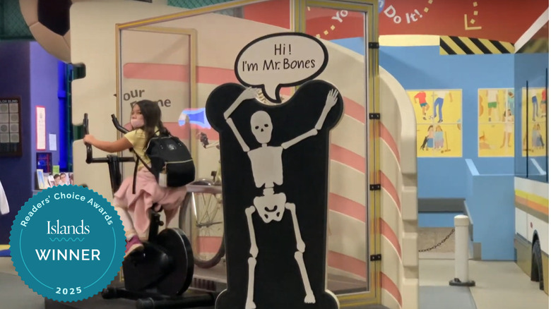 A girl pedaling on a bike next to a sign of a skeleton