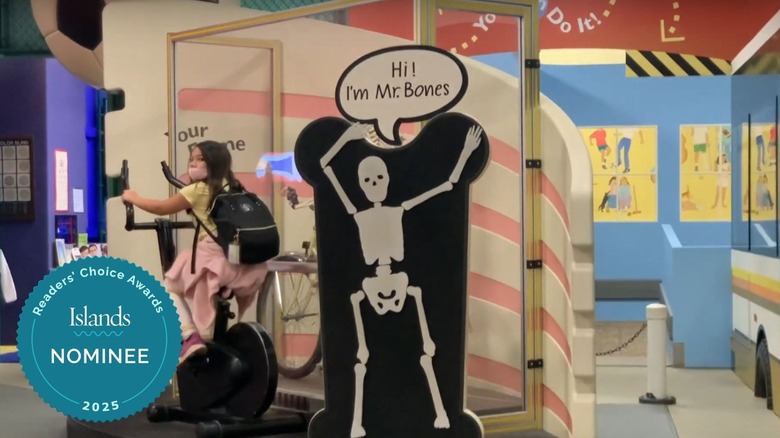 A girl pedaling on a bike next to a sign of a skeleton