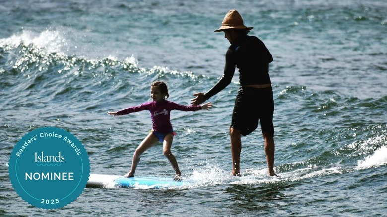 Little girl riding a surfboard with the help of an instructor