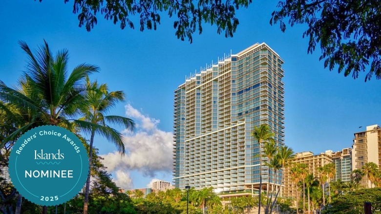 The multi-story Ka La'i Waikīkī Beach against a blue sky surrounded by palm trees and other buildings