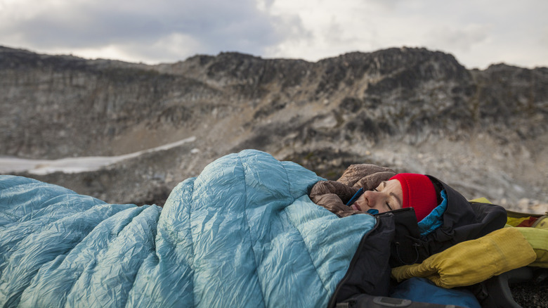 A woman sleeping in a sleeping bag outdoors in the mountains