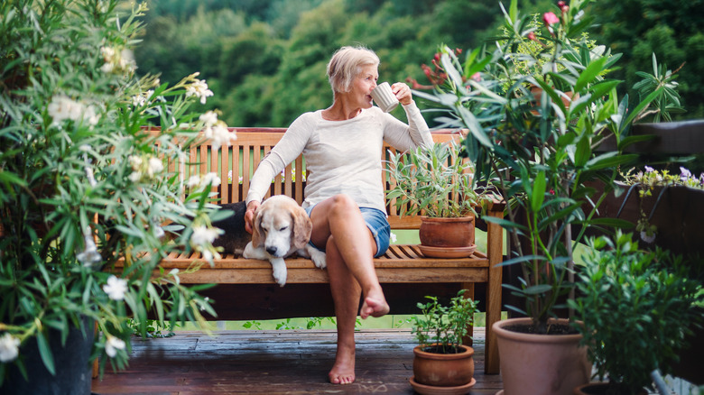 Woman drinking coffee on a wood bench with a dog