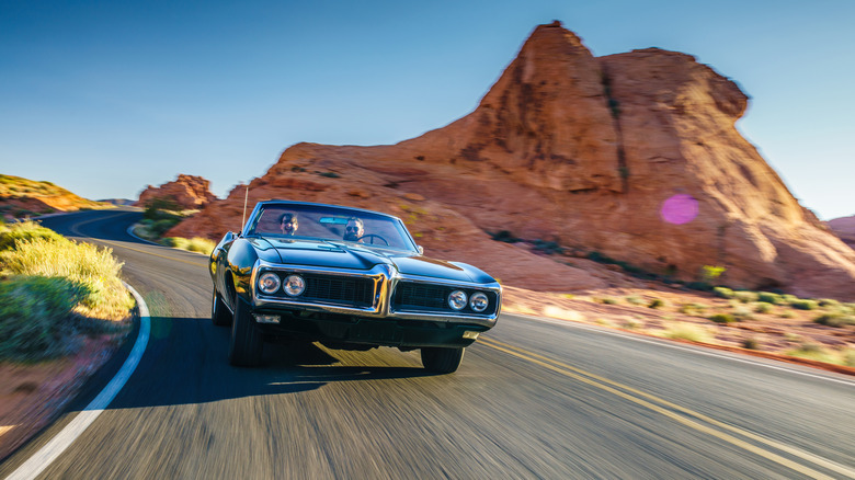 Two people driving on a road trip in a classic convertible car