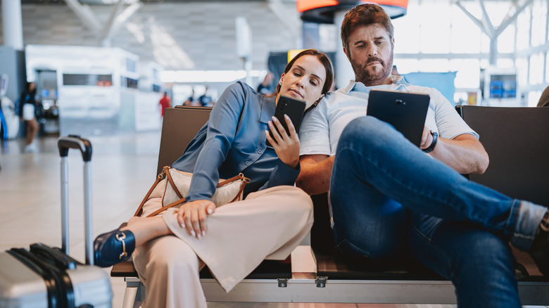 A couple waiting at the airport while engrossed in their technology