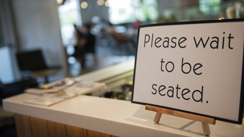 Sign that reads "please wait to be seated" in a restaurant