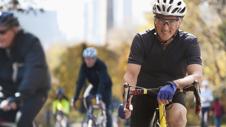Smiling senior wearing a helmet on a road bike in New York City with fellow bikers in the background