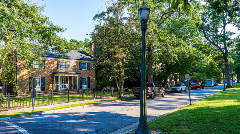 Quiet street with a brick house surrounded by trees and a black fence, Tarboro