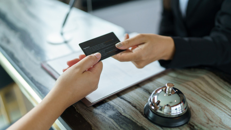 A hotel receptionist in uniform hands a key card to a guest at the front desk.