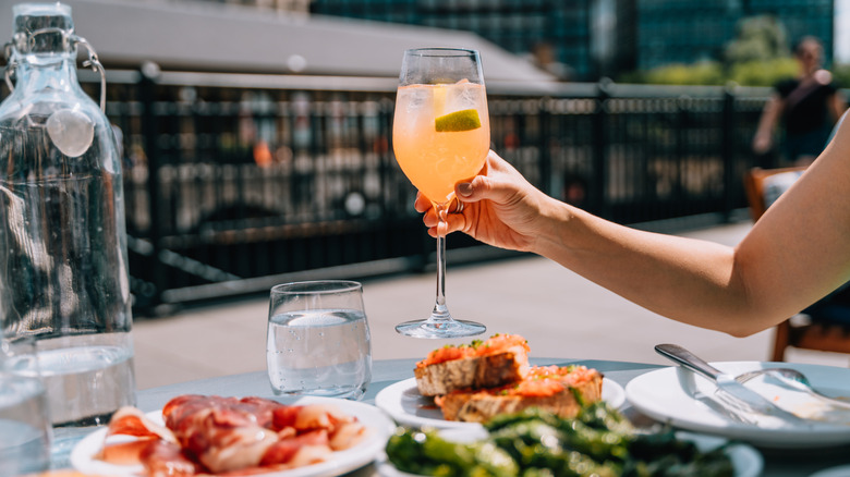 An arm holding a fizzy drink over a plate of food in a European setting