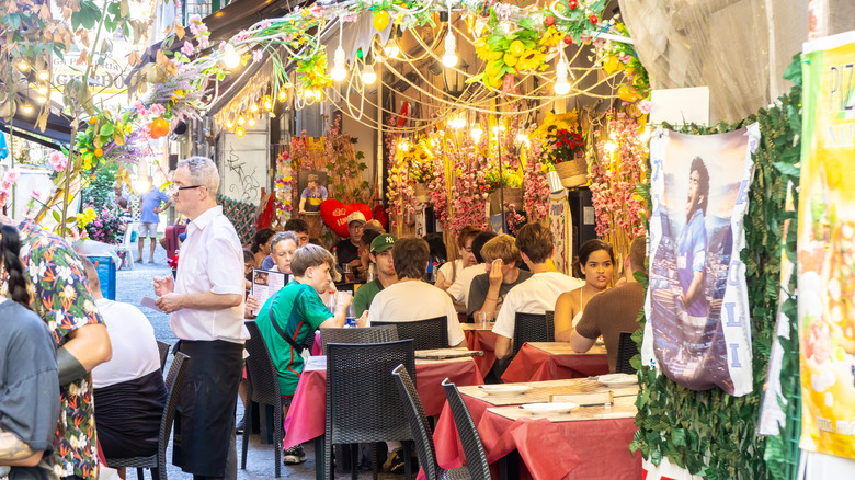 A server takes orders from tourists at a sidewalk restaurant in Europe