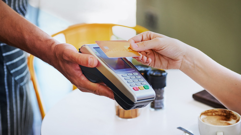 A hand pays for a transaction on a credit card machine held by a server's hand
