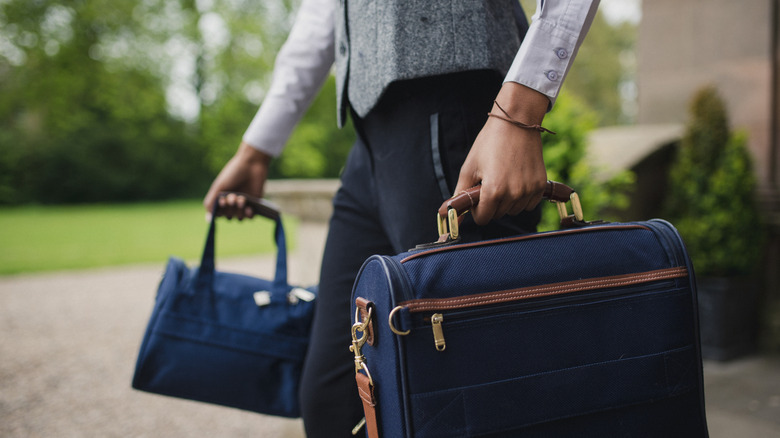 Cropped image of a porter in uniform carrying two pieces of baggage