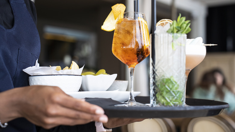 A server's hands carry a tray full of snacks and cocktails