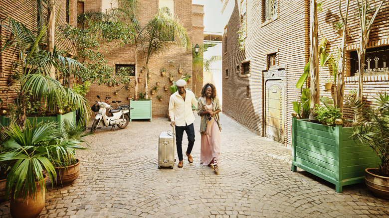 Couple walk in courtyard with rolling suitcase to hotel