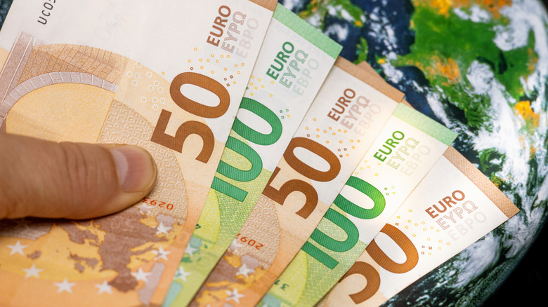 Hand holds Euros over world map