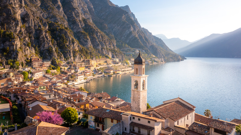 A view over a town next to Lake Garda's, the buildings and limestone cliff faces behind them reflected in the lake's placid waters