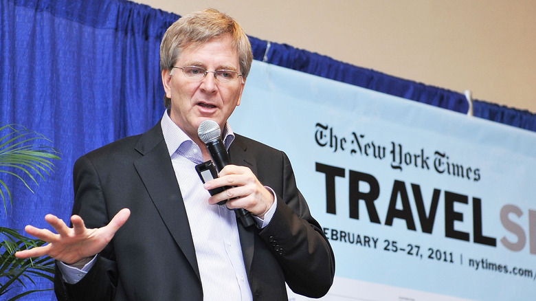 Rick Steves holding microphone speaking at New York Times Travel Show