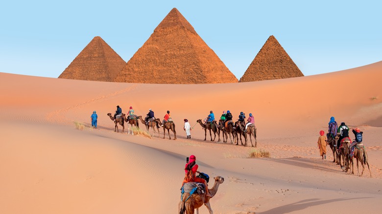 Tourists riding camels through desert toward Great Pyramids