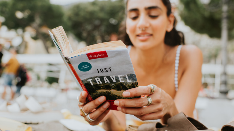 Woman laying on stomach reading travel guidebook