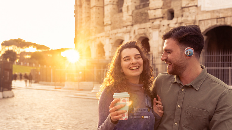 A traveling couple smiling and drinking coffee as they tour the city near the Coliseum in Rome, Italy.