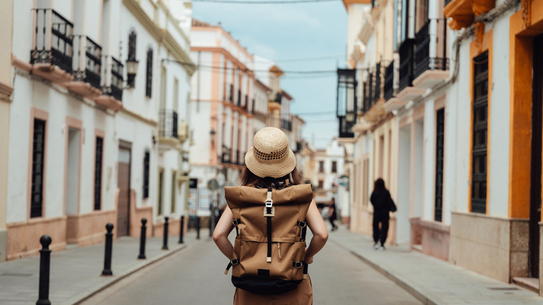 The back of a woman wearing a backpack standing alone in a street