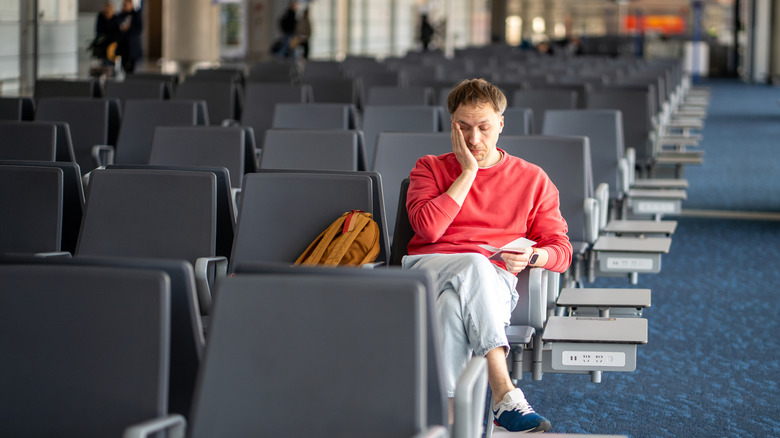 A tired traveler is falling asleep sitting up with his face in his hand in an airport terminal