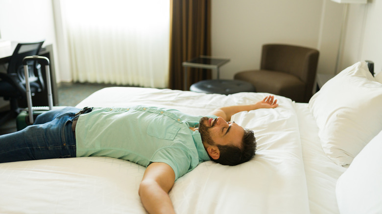 A traveler, just arrived at his hotel, is lying on a hotel bed in broad daylight