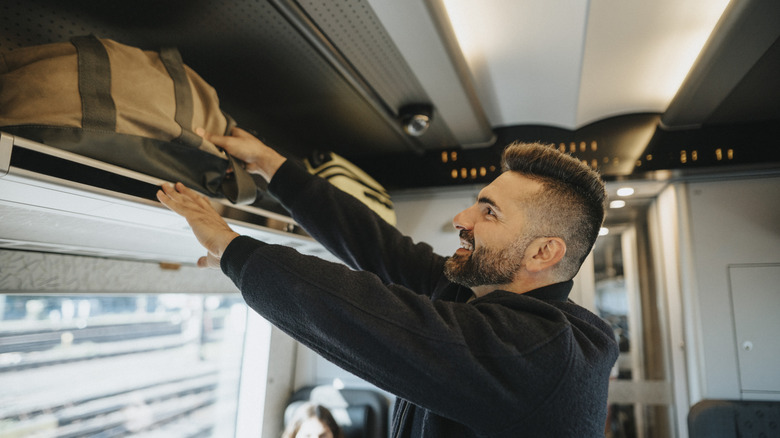 Traveler stowing his luggage in an overhead bin