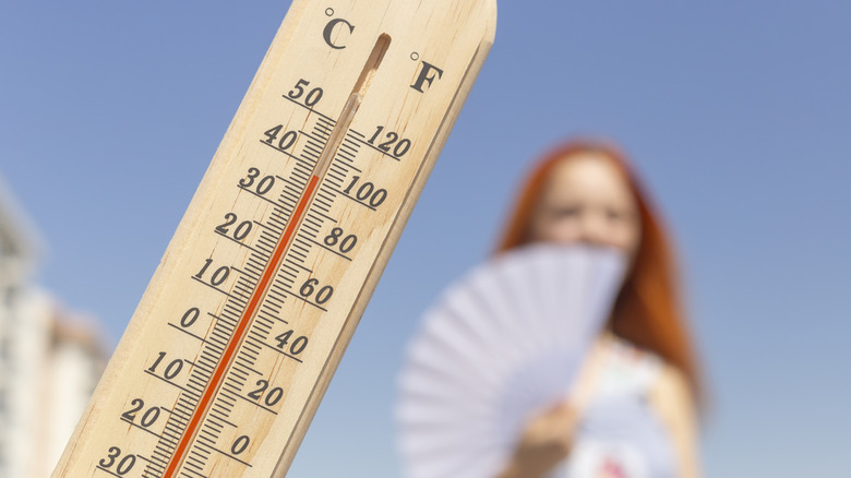 Thermometer in the foreground with blurry woman fanning herself in the background