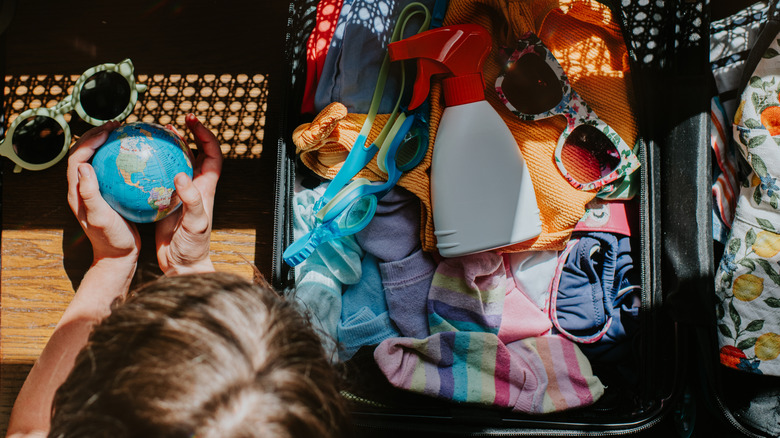 A child holds a small globe while packing a carry-on suitcase
