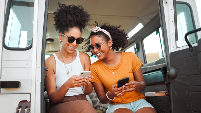 Two women use their mobile phones for travel planning while in camper van