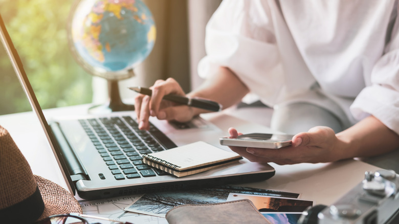A young traveler plans a vacation by searching for information on her mobile phone and laptop.