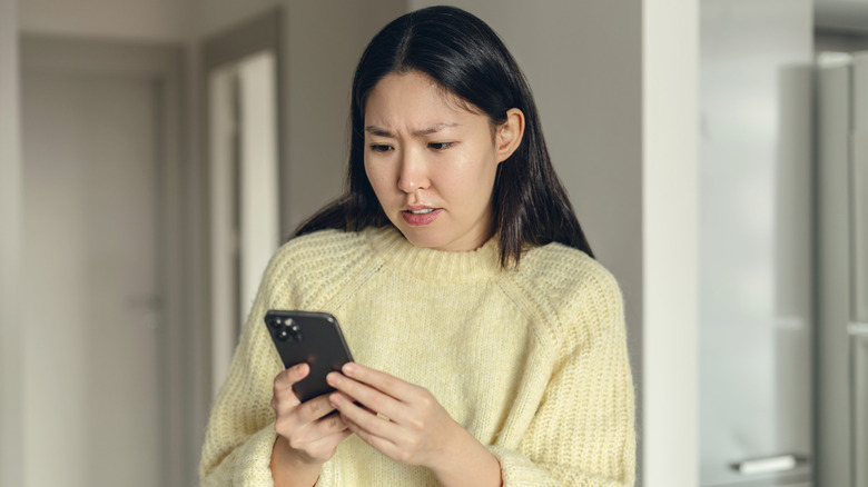Woman typing on a smartphone with a concerned facial expression