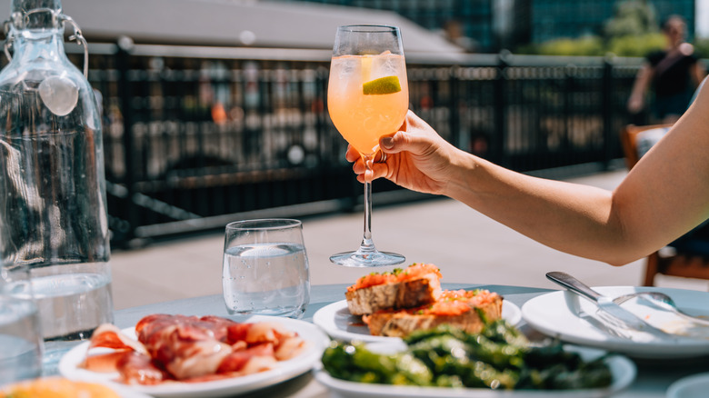 An arm holding a fizzy drink over a plate of food in a European setting