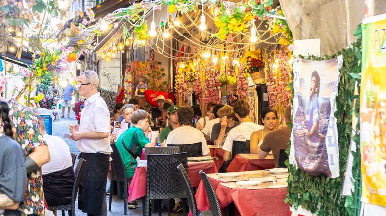 A server takes orders from tourists at a sidewalk restaurant in Europe