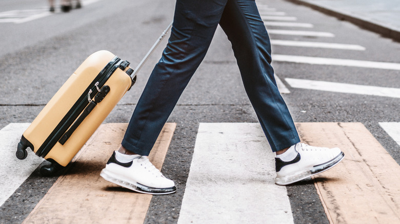 Person crossing a city street while pulling a yellow suitcase