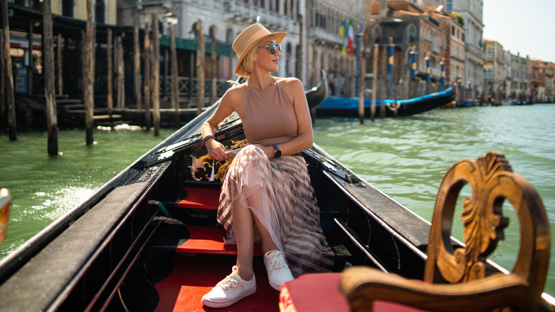 A woman in a hat and skirt sitting in a gondola in Venice, Italy.