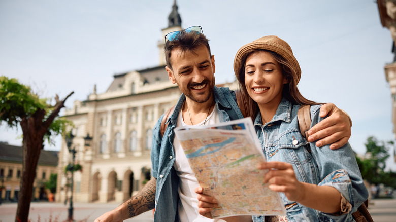 A young couple holding a map and suitcase in a European country.