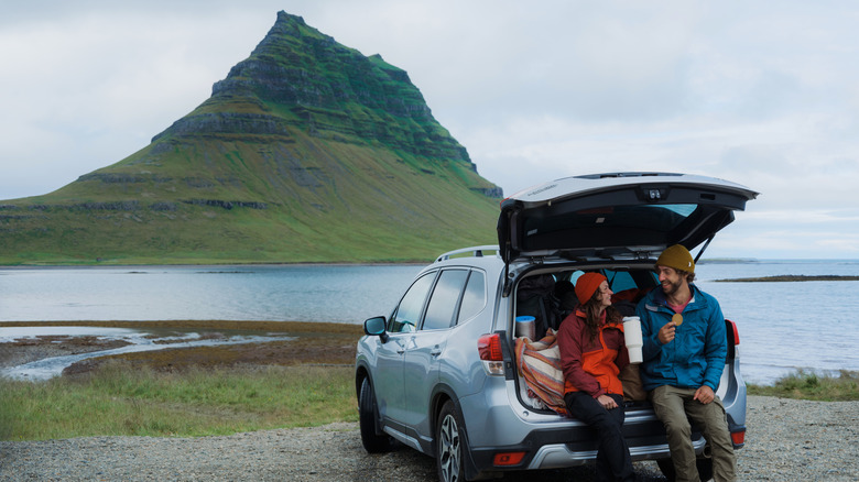 Couple sitting on open car trunk on a road trip break in Iceland