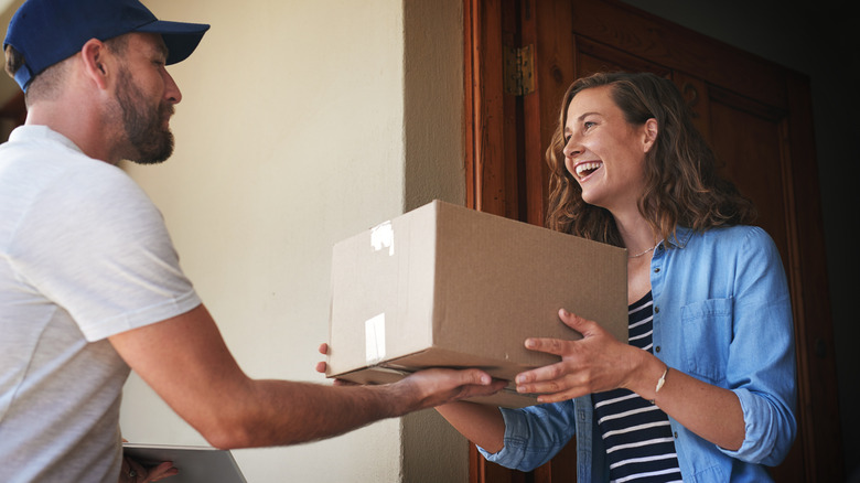 A man in cap handing a woman a package at her home.