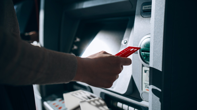 A hand hovers a card near the slot of an ATM machine