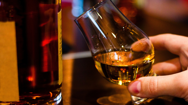 Hand tilting small glass of whisky
