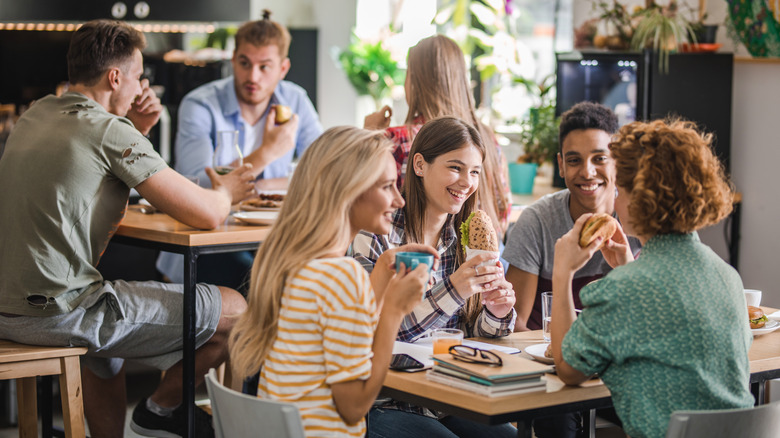 University students smiling and sitting around a uni cafeteria table eating lunch.