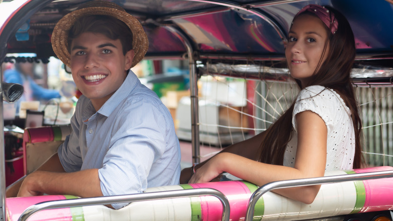 A smiling couple sitting in the back of a tuktuk