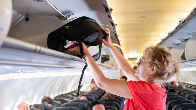 Woman puts backpack in airplane overhead bin
