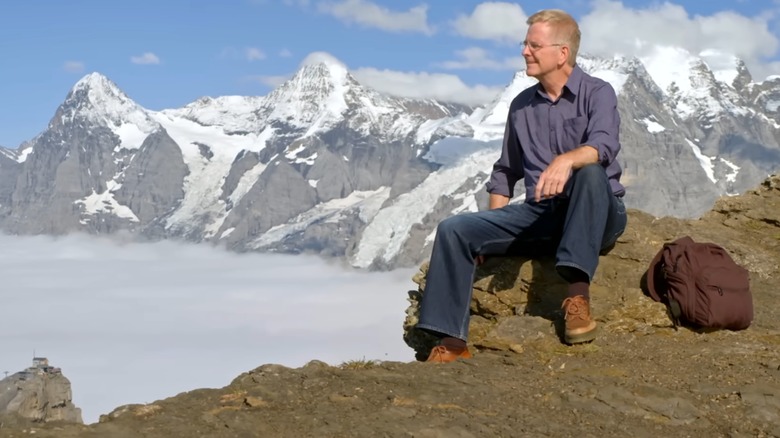 Rick Steves in the Alps, sitting next to a brown backpack