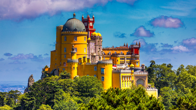 The bright yellow castle walls of Pena Palace, with red towers behind, green trees, and blue skies