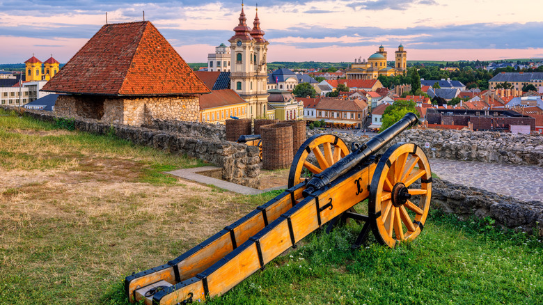 Wooden medieval canon on castle wall faces bright buildings of Eger during sunset