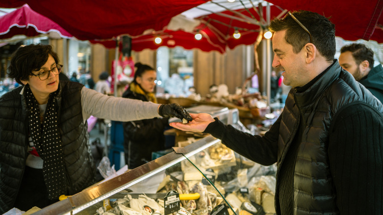 a man samples cheese from a vendor in a French market